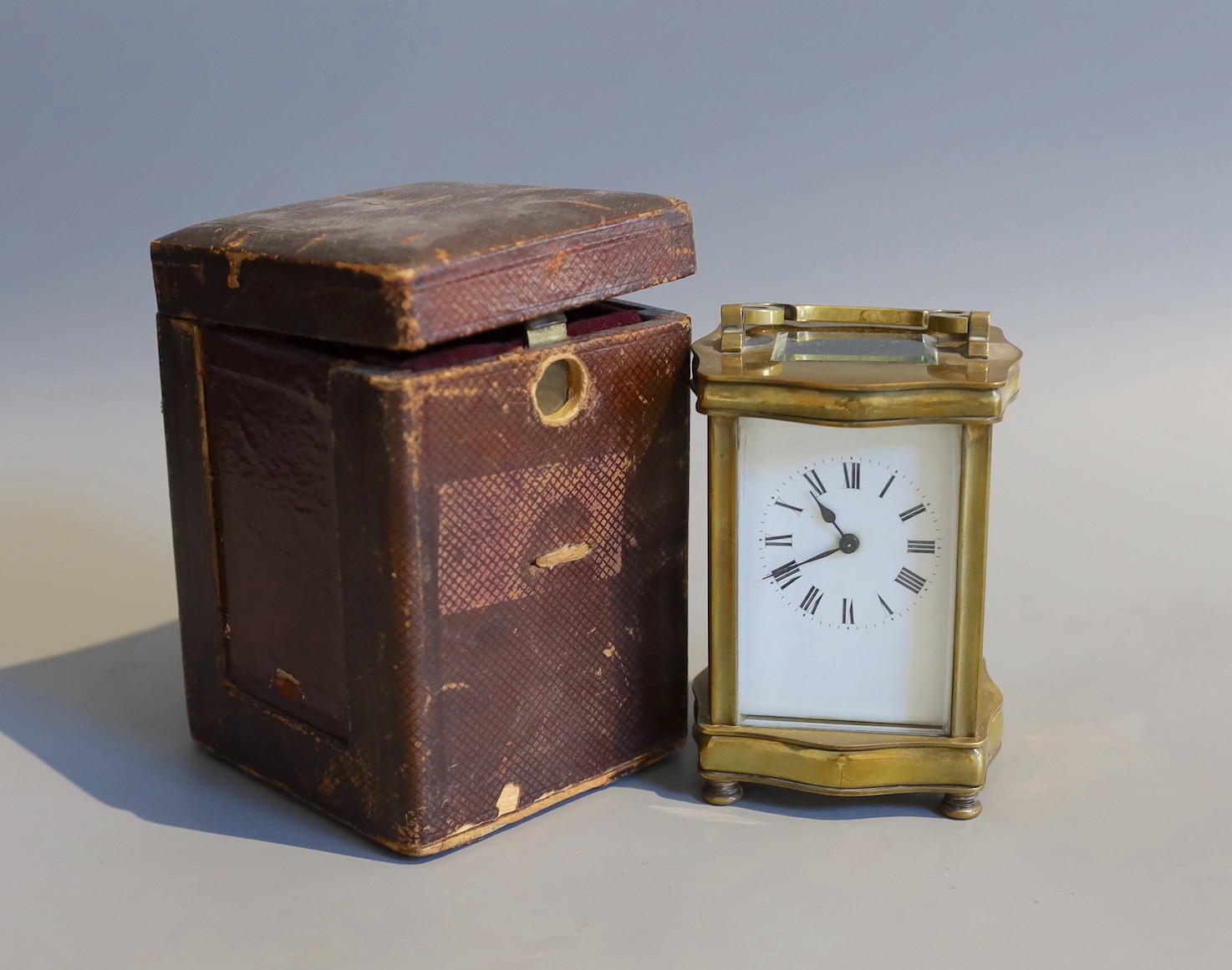 An early 20th century French lacquered brass carriage timepiece, of serpentine form, in red morocco case, height 12cm